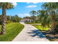 Beautiful home on a large lot, featuring lush landscaping and a long driveway, surrounded by mature trees and blue skies at 1785 Bayshore Dr, Englewood, FL 34223