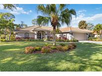 Charming home featuring lush landscaping, tile roof, and a well-manicured lawn with a large central palm tree at 7324 Links Ct, Sarasota, FL 34243