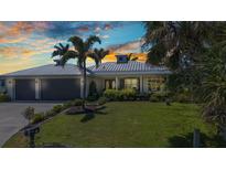Stunning single-story home featuring a metal roof, well manicured lawn and lush tropical landscaping at 18382 Arapahoe Cir, Port Charlotte, FL 33948