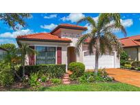 Charming single-story home with a terracotta tile roof, lush landscaping, and a brick paver driveway at 23823 Waverly Cir, Venice, FL 34293