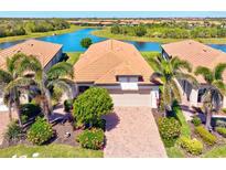 Stunning aerial view of a home with a tile roof, two-car garage, and lush landscaping near a scenic lake at 10064 Cozy Grove Dr, Venice, FL 34293