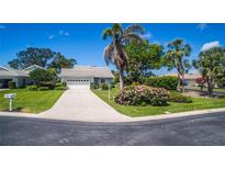 Charming home featuring a well-manicured lawn, flowering shrubbery, and a long driveway leading to a two-car garage at 1400 Colony Pl, Venice, FL 34292