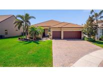 Charming single-story home featuring a red tile roof, brick driveway, and lush landscaping with tropical palm trees at 13897 Umbria St, Venice, FL 34293