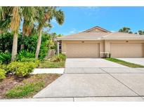 Beige home featuring a two-car garage, tile roof and palm trees in a well-maintained Florida neighborhood at 335 Auburn Woods Cir, Venice, FL 34292