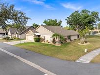 Charming single-story home with a well-manicured lawn and mature trees under a blue sky at 500 Wekiva River Ct # 129, Englewood, FL 34223