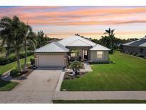 Charming single-story home featuring lush landscaping, a metal roof, and a two-car garage, all under a vibrant sunset sky at 19893 Cobblestone Cir, Venice, FL 34292