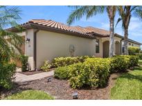 Beige one-story home featuring a clay tile roof, lush landscaping, and a brick walkway at 115 Babbling Brook Run, Bradenton, FL 34212