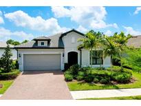 Charming single-story home with a brick driveway, lush landscaping, and a gray tiled roof at 1565 Hyssop Loop, North Port, FL 34289
