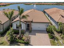 Charming single-story home with a paved driveway and a serene waterfront view of a lake with a fountain at 149 Vinadio Blvd, Nokomis, FL 34275