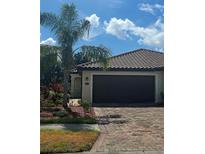 Charming home featuring a clay tile roof, brick driveway and tropical landscaping with a palm tree in front at 20188 Tesoro Dr, Venice, FL 34293
