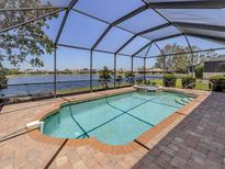 A screened-in pool featuring a spa and a view of the water, with a brick patio at 11610 Dancing River Dr, Venice, FL 34292