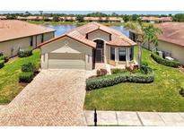 Inviting single-story home with a red tile roof, manicured lawn, and a brick driveway leading to the garage at 20246 Pezzana Dr, Venice, FL 34292