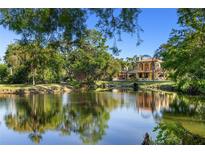 Stunning view of estate home overlooking a serene pond surrounded by mature trees on a sunny day at 2750 Gocio Road Ext, Sarasota, FL 34235