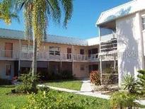 Two-story condo building featuring white exterior, balconies, green lawn, and mature trees, offering a serene living environment at 400 Base # 225, Venice, FL 34293