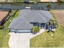 An aerial view of a home's facade, showing a well-manicured lawn, palm trees, three-car garage, and waterfront location at 15448 Avery Rd, Port Charlotte, FL 33981