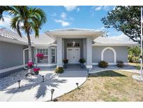 Inviting front entrance with double doors, bright flowers, swaying palm tree, and white gravel at 1568 Ringtail Rd, Venice, FL 34293