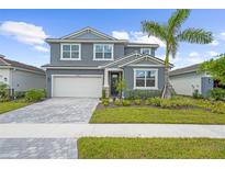 Charming two-story home featuring a gray facade, well-manicured lawn, and a brick-paved driveway leading to a two-car garage at 18001 Grand Prosperity Dr, Venice, FL 34293