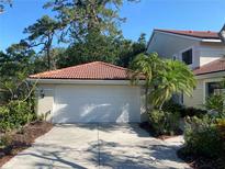 Two-car garage with white door and red tile roof, surrounded by lush landscaping and a concrete driveway at 7560 Fairway Woods Dr # 305, Sarasota, FL 34238