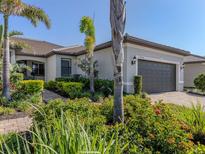 Beautiful single-story home with lush landscaping, palm trees and a brick driveway leading to the two-car garage at 13908 Vadini St, Venice, FL 34293