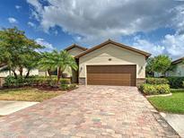 Charming single-Gathering home featuring a paver driveway, two car garage, and tropical landscaping at 12728 Richezza Dr, Venice, FL 34293