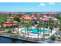 Stunning aerial view of the community pool and clubhouse with palm trees and ocean views beyond the red tile roofs at 97 Vivante Blvd # 306, Punta Gorda, FL 33950