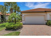 Charming home exterior with a red tile roof, brick driveway, and beautiful tropical landscaping at 9823 Haze Dr, Venice, FL 34292