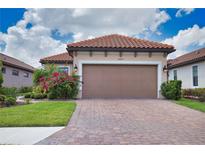 Home featuring a two-car garage, brick paved driveway and exterior landscaping with bougainvillea at 10410 Inglenook Ter, Palmetto, FL 34221