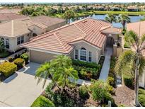 Beautiful home with a red tile roof, lush landscaping, and a serene lake view at 165 Tiziano Way, North Venice, FL 34275