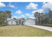 Charming single-story home featuring lush lawn, palm trees, and a two-car garage, showcasing curb appeal at 27416 Natal Dr, Punta Gorda, FL 33983