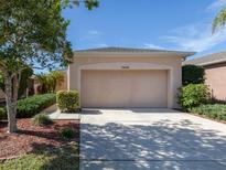 Beige two car garage with an arched top, lush landscaping, and visible house number on a sunny day at 11649 Tempest Harbor Loop, Venice, FL 34292