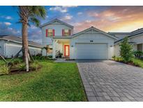 Charming two-story home featuring a paved driveway, well-manicured lawn, and a bright orange front door at 12816 Morning Mist Pl, Venice, FL 34293