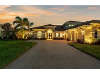 Elegant home exterior featuring a brick driveway, well-manicured lawn, and a beautifully illuminated facade at sunset at 186 Portofino Dr, Nokomis, FL 34275
