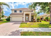 Two-story home featuring a two-car garage, a welcoming front porch, and a well-manicured lawn with beautiful landscaping at 11986 Granite Woods Loop, Venice, FL 34292