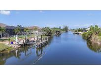 Scenic waterfront view featuring a private dock and canal access, surrounded by lush landscaping and clear blue skies at 14398 Fort Worth Cir, Port Charlotte, FL 33981