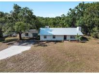 Charming single-story home with a white metal roof, surrounded by mature trees and a gravel driveway at 2008 55Th E Ave, Bradenton, FL 34203