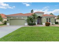 Charming green home featuring a well-manicured lawn, desert landscaping, and a red tile roof at 6619 Pinefeather Ct, Bradenton, FL 34203