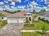 Beautiful home with a tile roof, three-car garage, and a lush lawn with manicured landscaping and brick paver driveway at 12404 Destin Loop, Venice, FL 34293