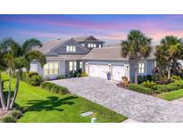Beautiful gray home featuring a three-car garage, lush landscaping, and a paver driveway at 8245 Grande Shores Dr, Sarasota, FL 34240