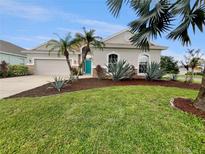 Charming home featuring a well-manicured lawn and vibrant landscaping with mature palm trees and a teal front door at 2302 123Rd E Pl, Parrish, FL 34219