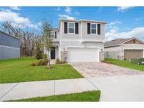 Two-story home featuring a two-car garage, paver driveway, stone accents, and manicured lawn at 37545 Mackenzie Dr, Zephyrhills, FL 33540