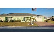 Charming one-story home with a green facade, mature landscaping, and a brick-paved driveway at 906 Bluewater Dr, Sun City Center, FL 33573