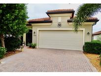 Charming home exterior with a two car garage, tile roof, brick driveway, and well manicured landscaping at 10088 Cozy Grove Dr, Venice, FL 34293