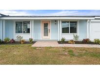 Charming home exterior featuring a light blue facade, a pink front door, and well-maintained landscaping at 511 Sharon Cir, Port Charlotte, FL 33952