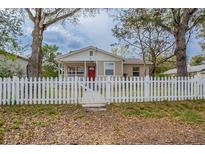 Charming single-story home featuring a red door, a white picket fence, and mature trees in the front yard at 3408 Phillips St, Tampa, FL 33619