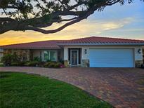 Charming single-story home with a red tile roof, stone accents, and a brick driveway at sunset at 1706 S Lakeside Ct, Venice, FL 34293