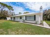 Inviting home featuring a white brick exterior, metal roof, and lush green lawn at 18526 Sweetbay Ln, Dade City, FL 33523