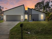 Contemporary home featuring modern architecture, a two-car garage, and well-manicured lawn at sunset at 24349 Kingsway Cir, Punta Gorda, FL 33983