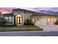 Elegant home featuring a three-car garage, arched entry, and manicured landscaping at 5516 Madrigal Way, Apollo Beach, FL 33572