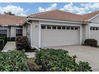 Beige house featuring a two-car garage with a tile roof and manicured landscaping at 1830 San Silvestro Dr, Venice, FL 34285