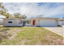 Charming single-story home featuring an attached garage, red front door, and a well-maintained lawn at 9811 Rainbow Ln, Port Richey, FL 34668
